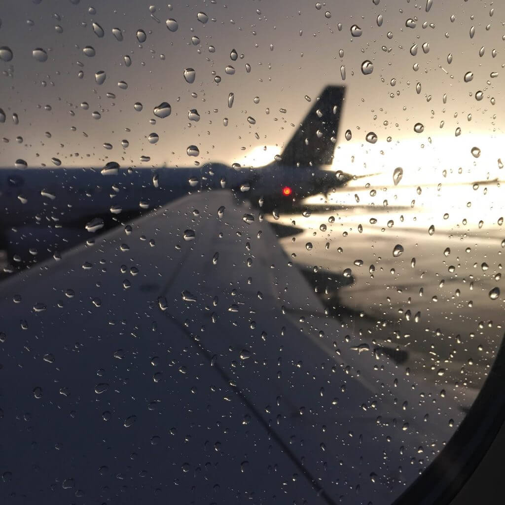 View from the window seat on my flight from Denver to Pittsburgh. Rain speckles the window and the sun sets in the background as the plane waits to take off.