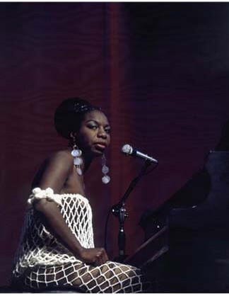 A photograph of Nina Simone sitting at a piano.