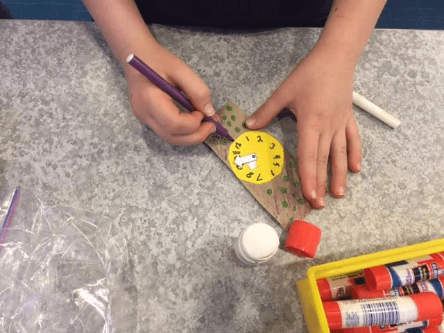 Child decorates watch craft with markers.