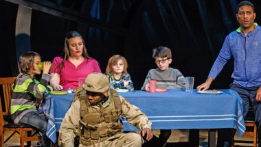 Soldiers crouch in front of a dinner table in the opera "The Long Walk."