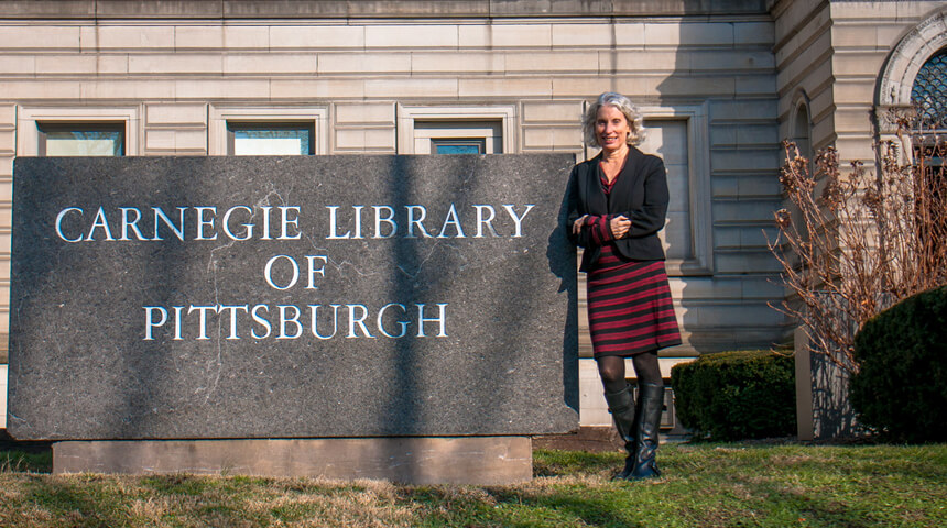 Mary Frances Cooper standing next to granite sign displaying "Carnegie Library of Pittsburgh"