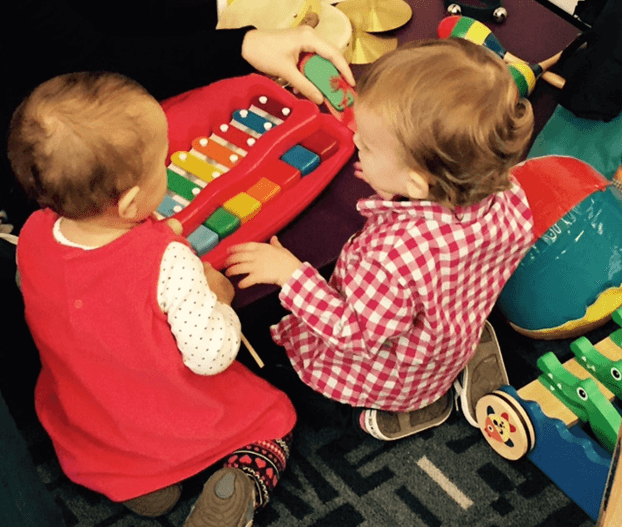 Two babies explore a xylophone held by a caregiver during Little Learners Playtime program