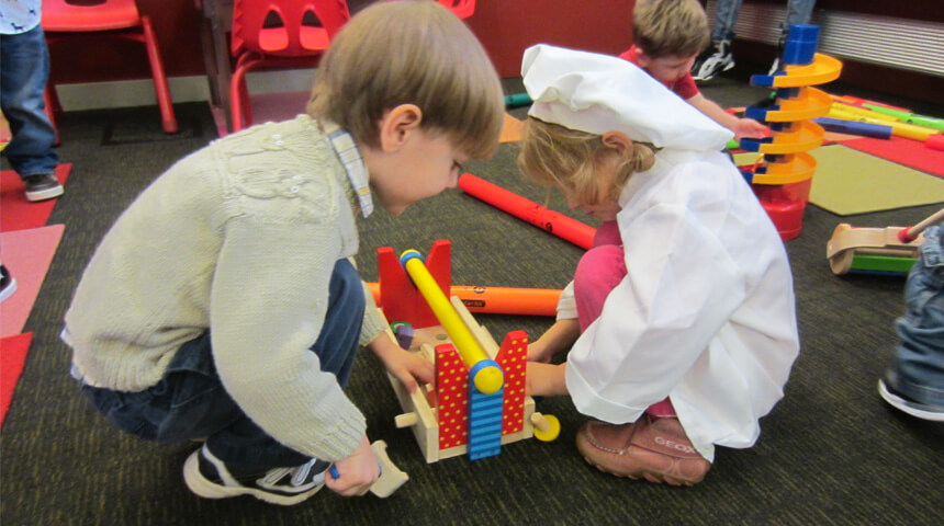 Two children play with a toy toolbox, with one child dressed in a chef's costume