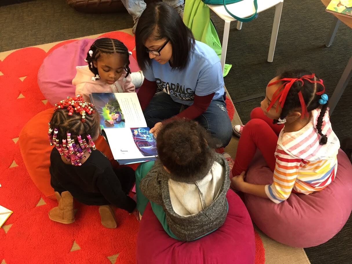 A children's librarian shows a picture book to four young children