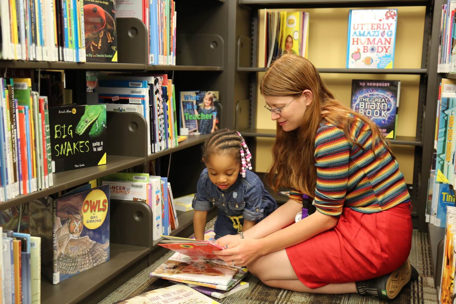 A young woman reads with a little girl in the library.