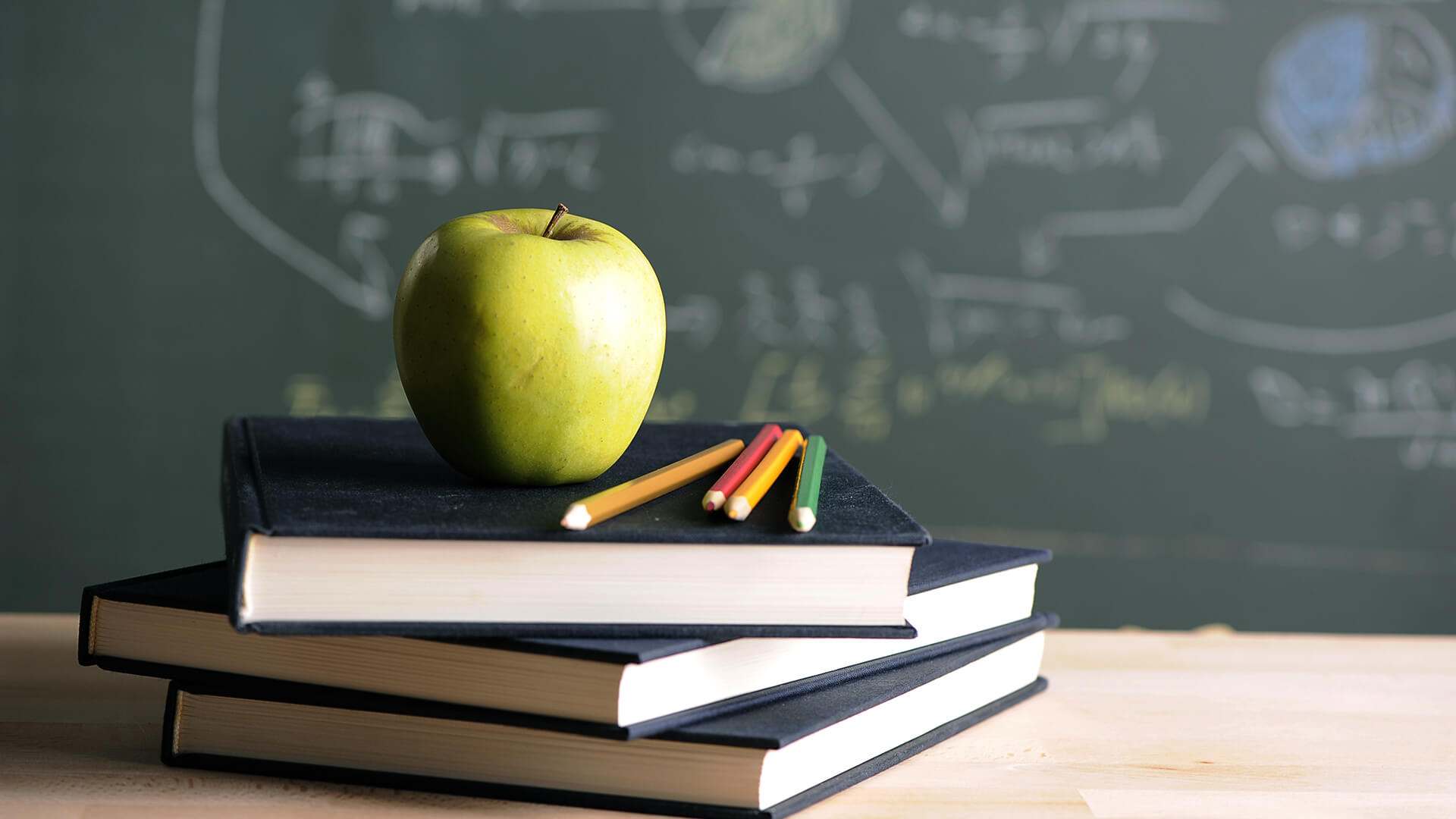 A green apple sitting on top of a stack of books in front of a chalk board