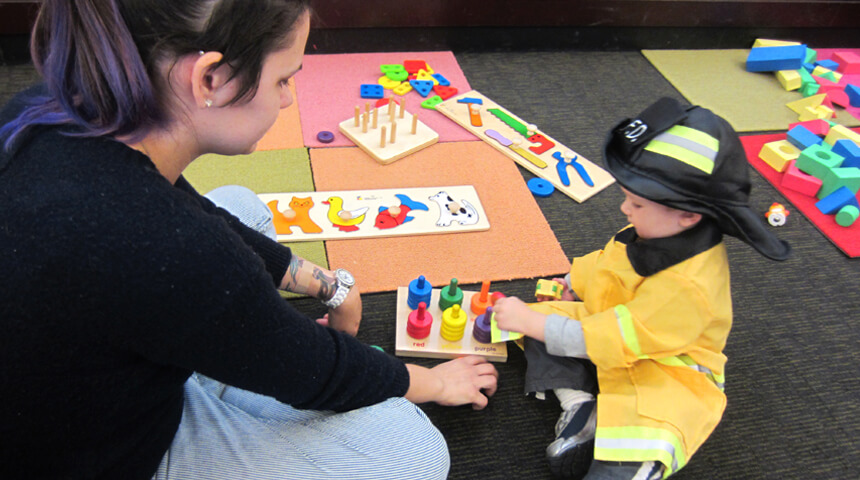 Adult and child in fireman costume play with puzzles in play area