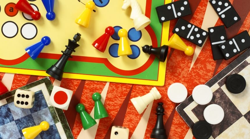 An array of tabletop game pieces and boards including dice, chess pieces, checkers and dominoes.