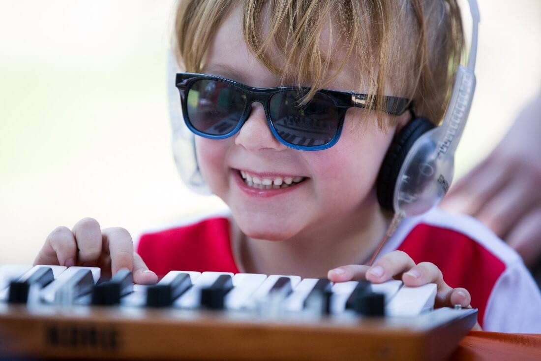 Child wears sunglasses and headphones while playing a keyboard