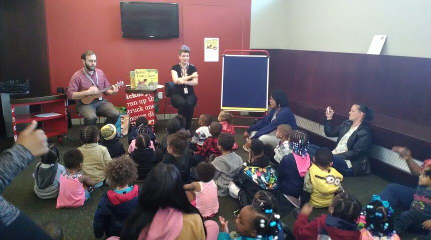 Two librarians lead large group of children in storytime