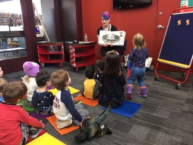 A librarian reads a book to ten children during storytime