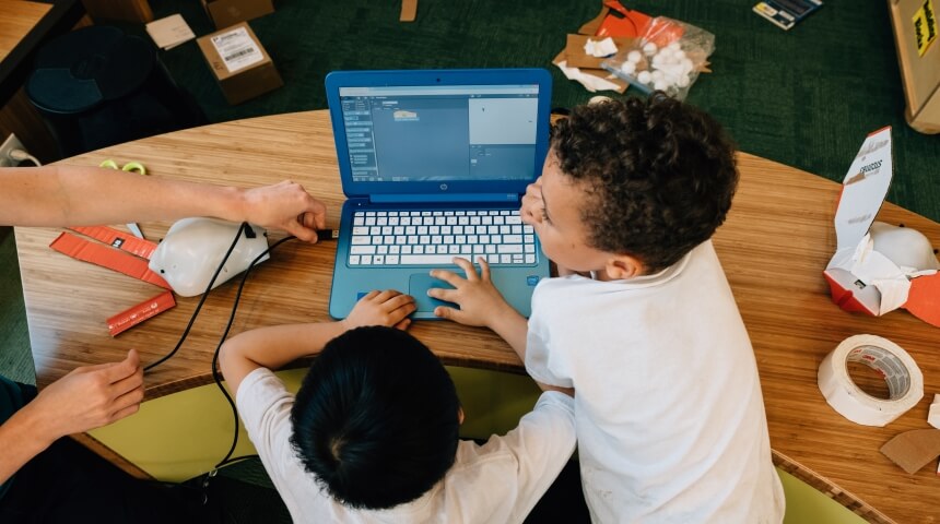 Two young children use a laptop computer together