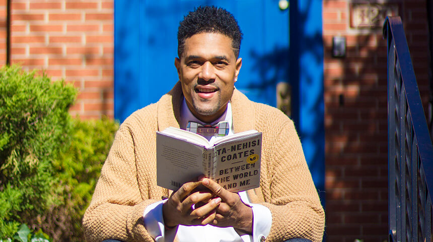 Emmai Alaquiva sitting in front of a blue door holding a book