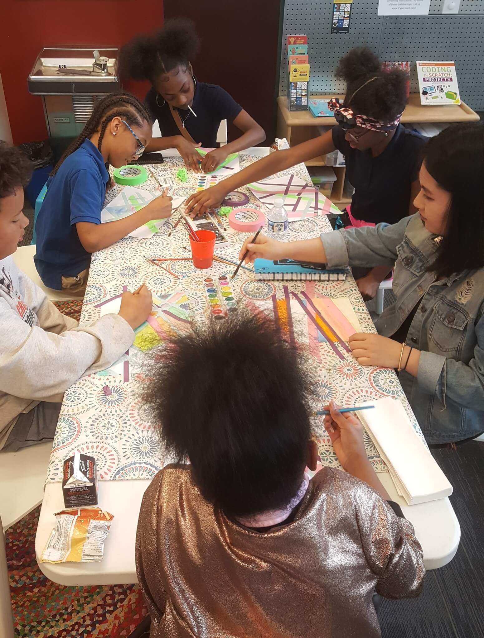 six tweens and teens sit around a table coloring