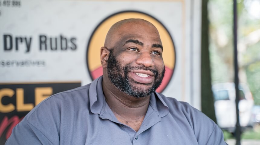 Jamal Etienne-Harrigan sits in his hot sauce booth at a local farmer's market