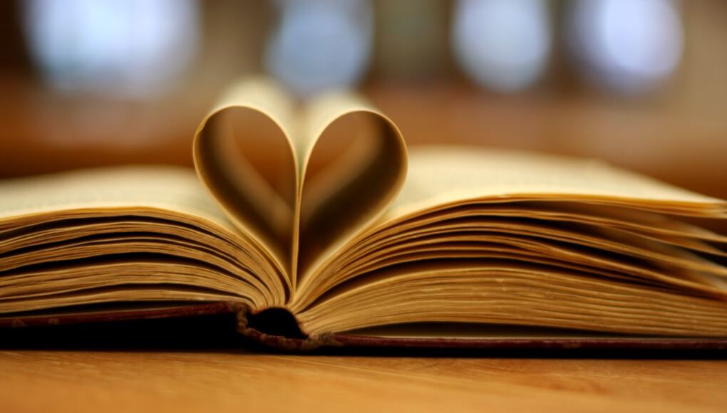 A book lays open on a table with some of the pages folded back to make a heart