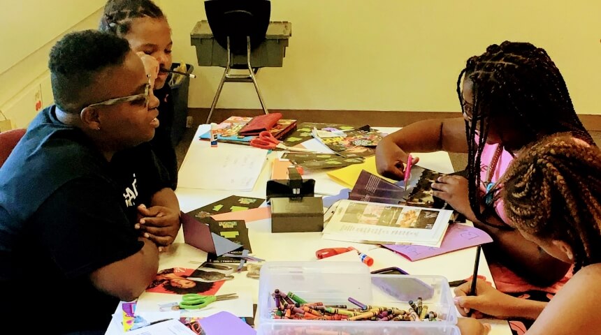 Library staff member and teens working on a craft at an outreach visit.