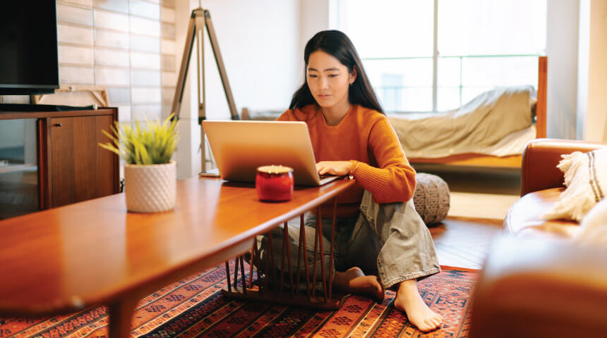 Person sitting on floor looking at a laptop on a coffee table.