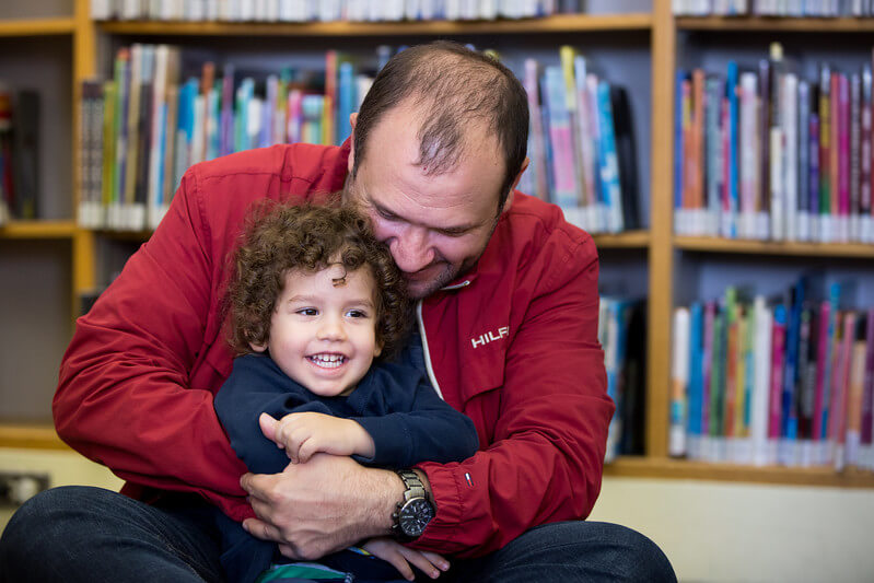 An adult in a red jacket and a child in a blue sweater snuggle at the Library.