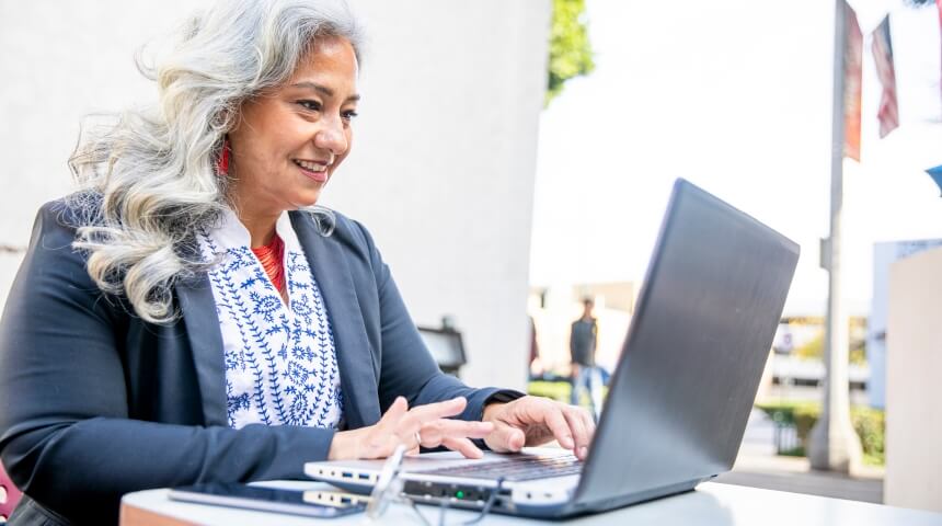Older woman smiling and typing on a laptop