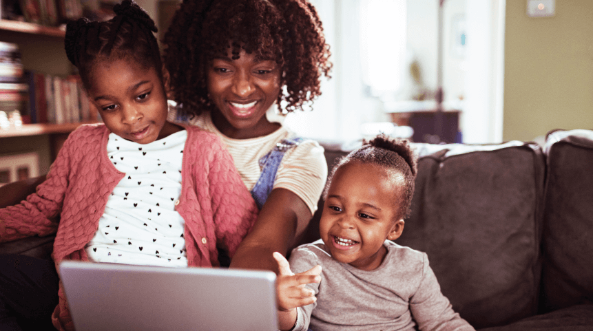 A parent and two children use a laptop together at home.