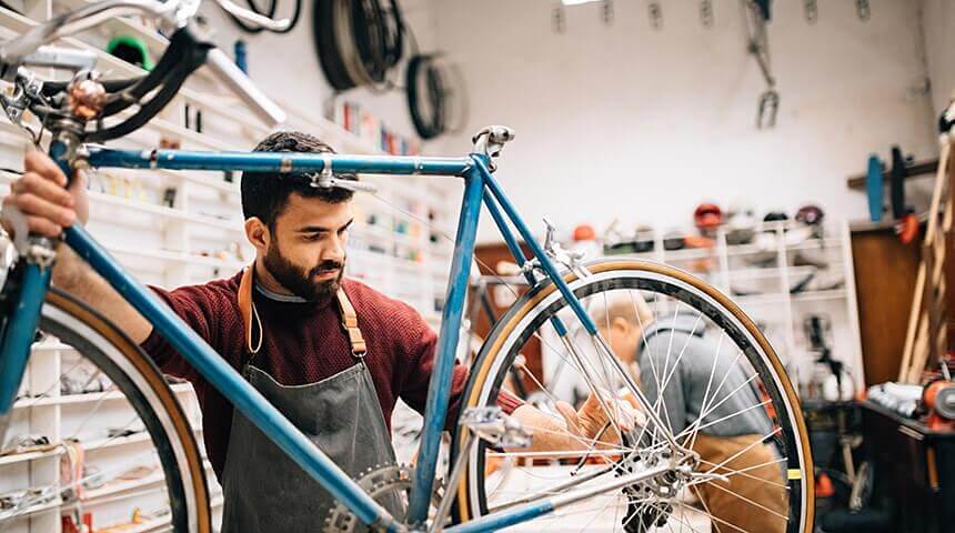 Person wearing an apron fixing a bicycle at their work bench.