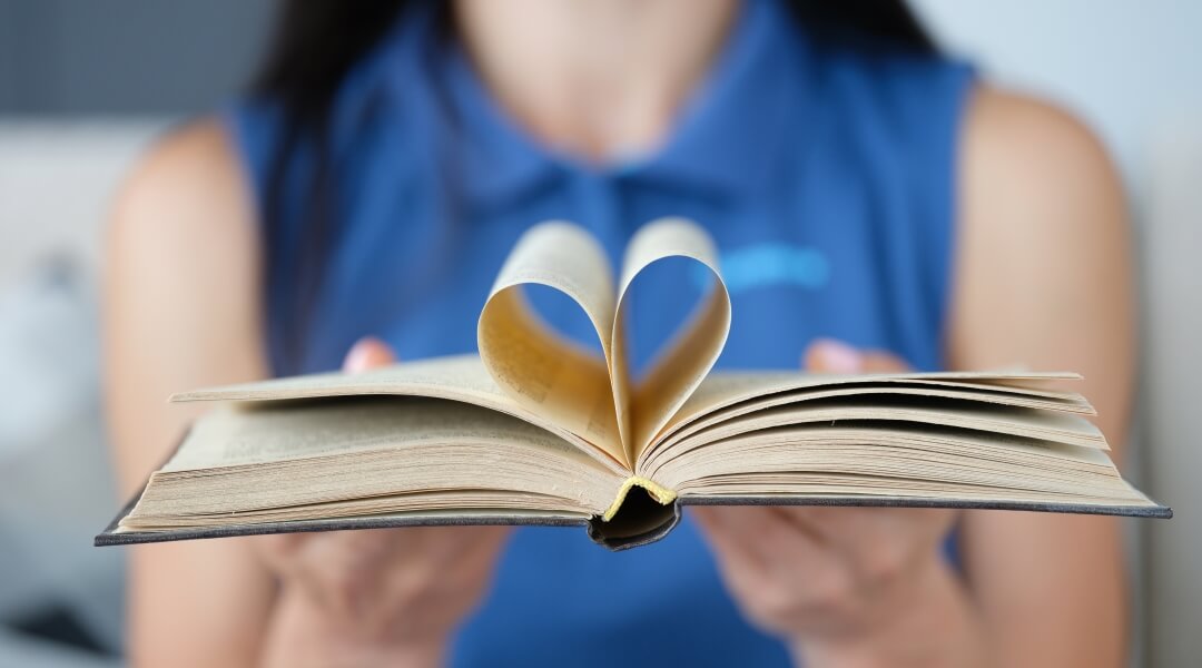 Person in blue shirt presenting a hardcover books with pages bent toward the spine to look like a heart