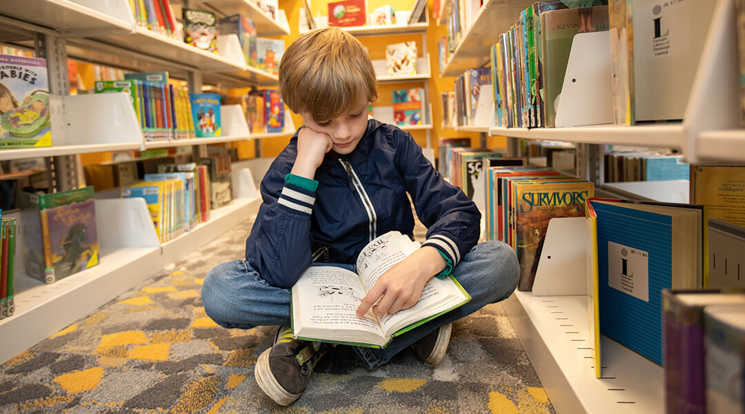Child sitting on the floor and reading a library book.