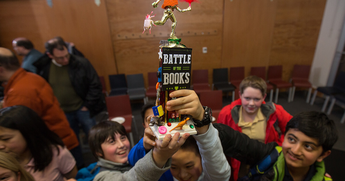 A group of middle school-aged kids holding up a Carnegie Library of Pittsburgh "Battle of the Books" trophy.