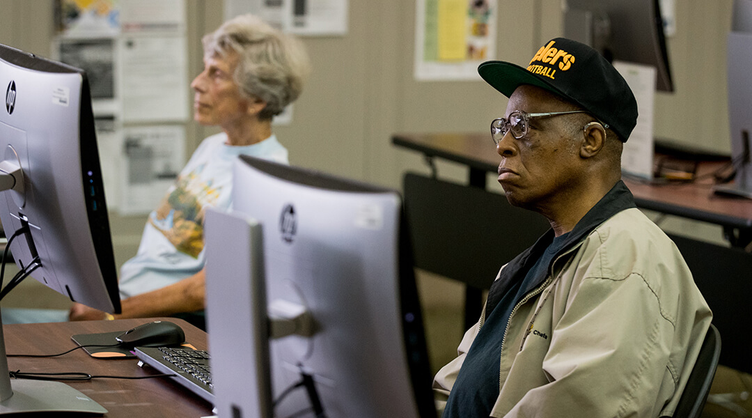 Two adults listening participating in a computer class at the library.