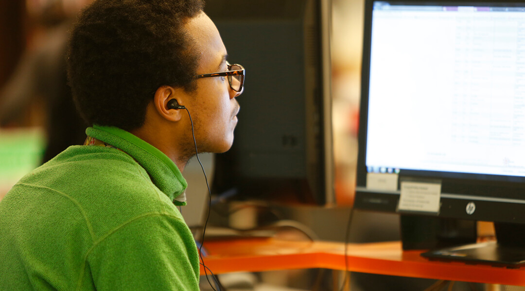 Young man wearing ear buds and looking at a library public computer