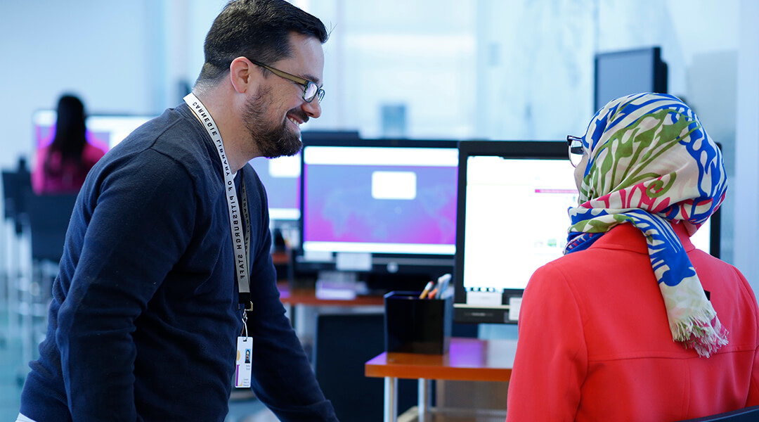 A librarian helps a patron at a public computer.