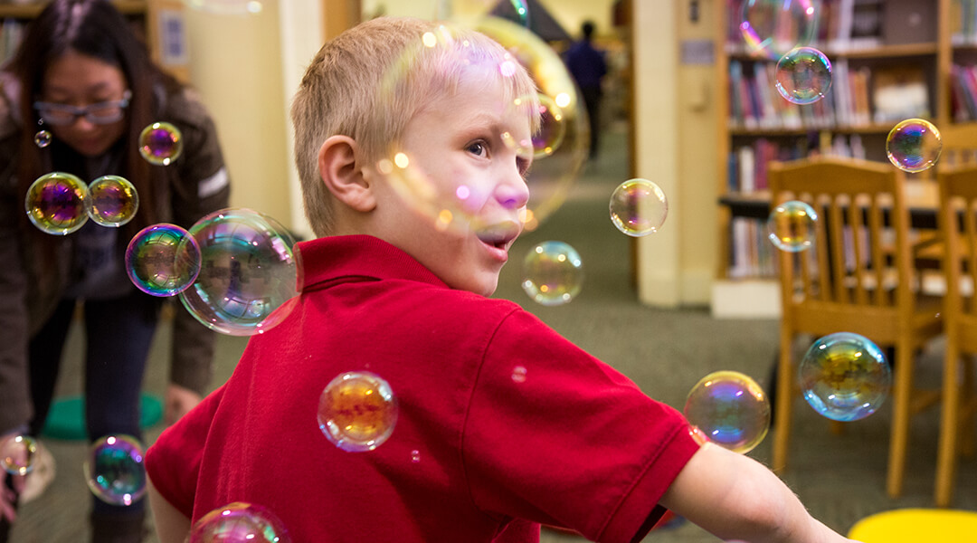 Child surrounded by bubbles at a library storytime.