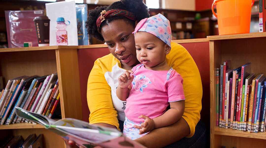 Caregiver and toddler reading a book together.