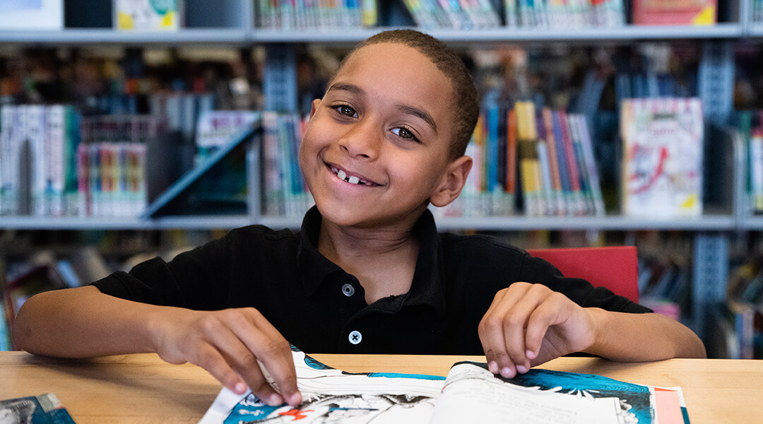 Child smiling and reading a book at CLP-Allegheny.