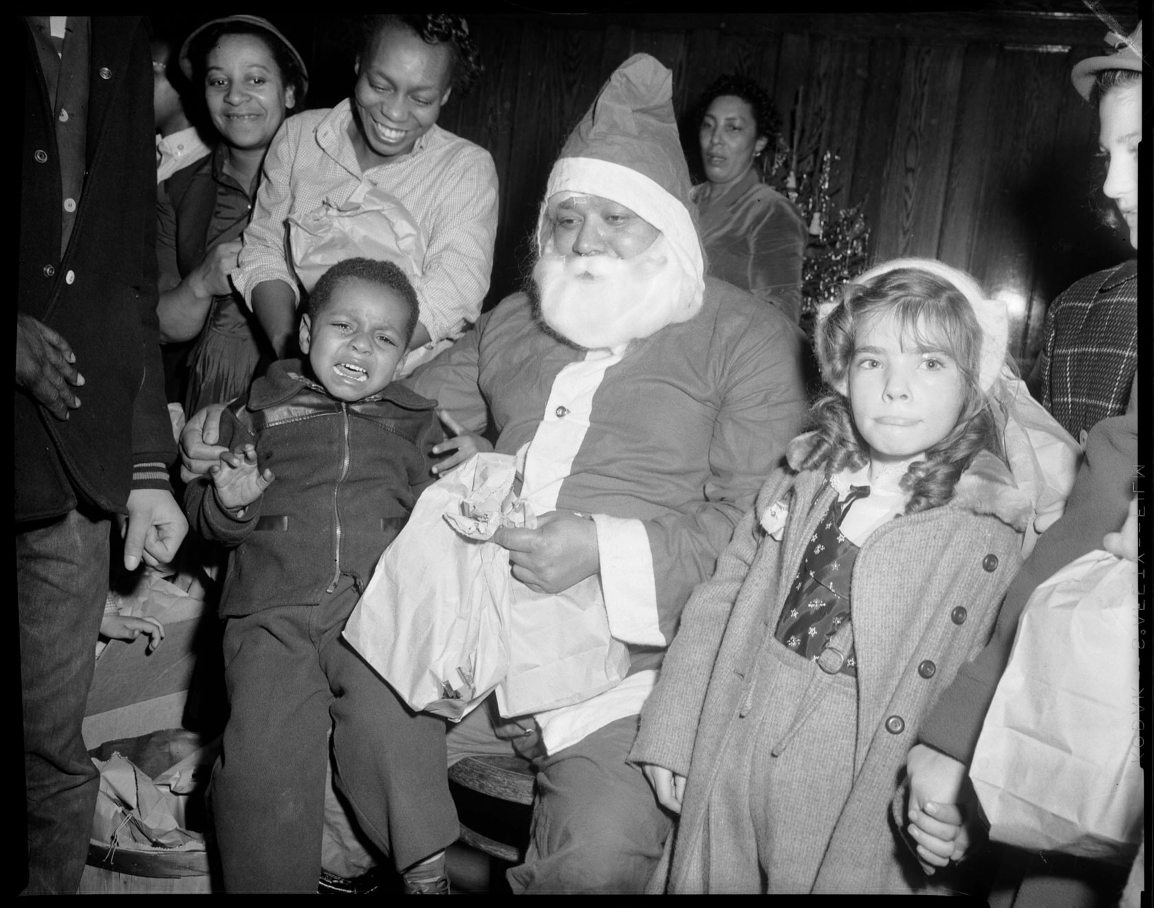 Child sits and cries on a fake Santa Claus's lap at the East Liberty library branch circa 1955.