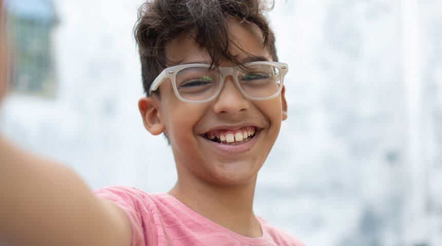 Child in pink shirt with white eyeglasses and big smile.