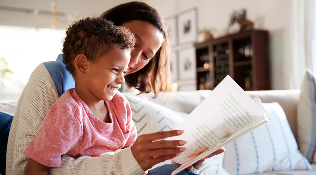 A smiling adult and young child reading a book together.