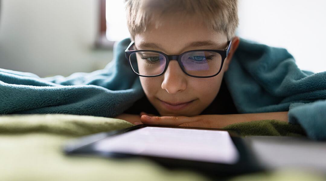A teen wearing glasses reading on a tablet