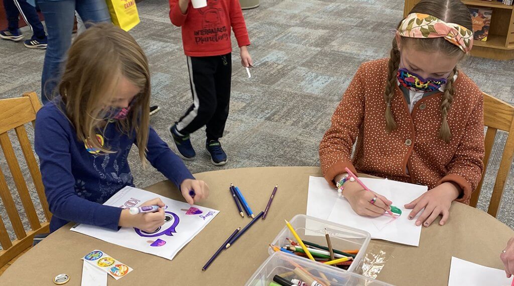 Two children wearing face masks and coloring with markers during a Kids Club program.