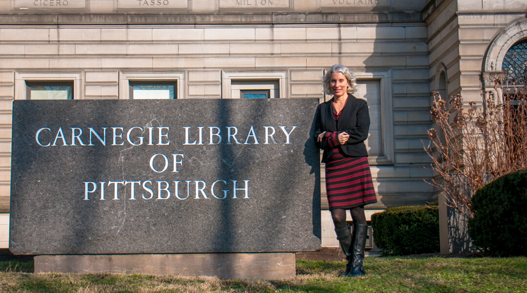 Mary Frances Cooper standing in front of CLP-Main, posing with the Carnegie Library of Pittsburgh sign.