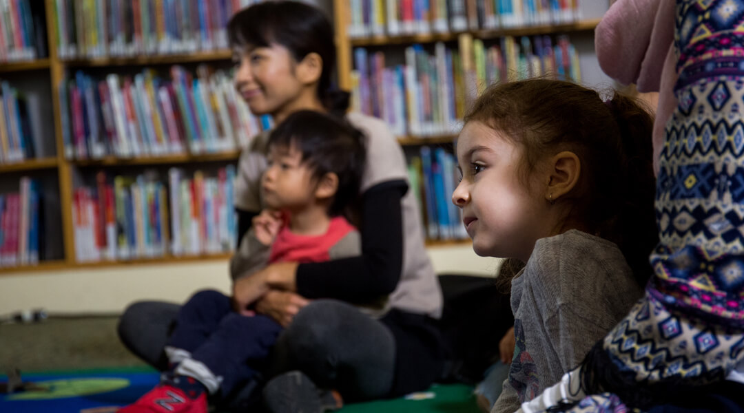 Toddlers sitting with caregivers during storytime.