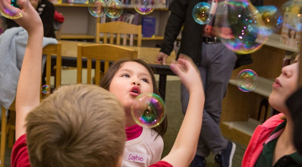 Young children playing with bubbles in a library.