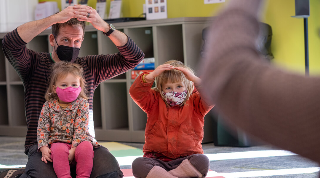 Babies and caregiver doing sing-along movements during storytime.