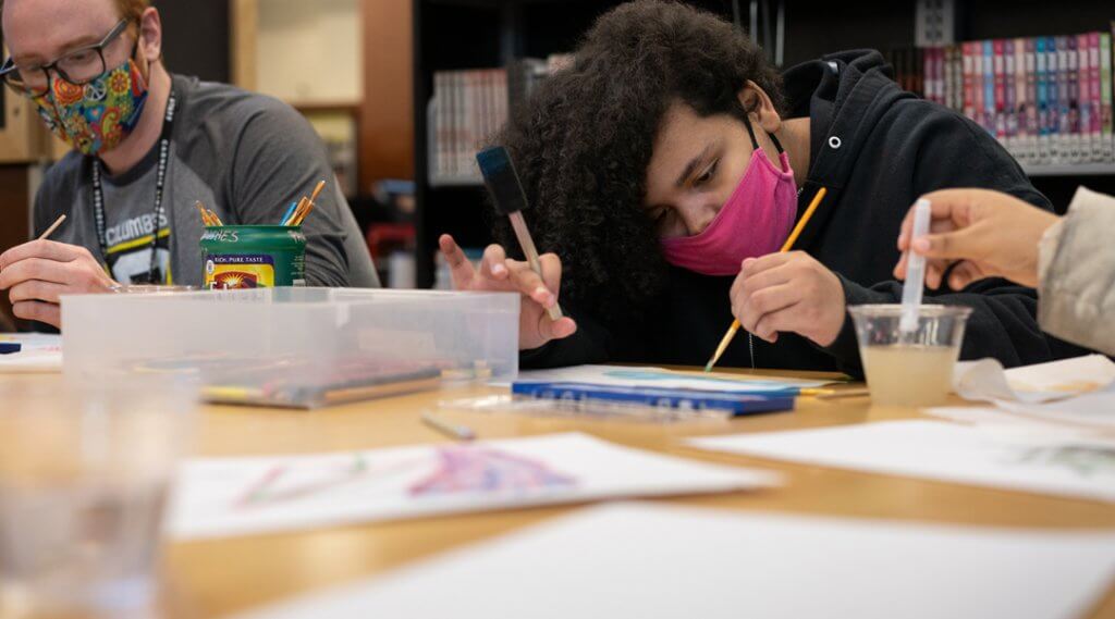 Teens wearing masks and painting in the library.