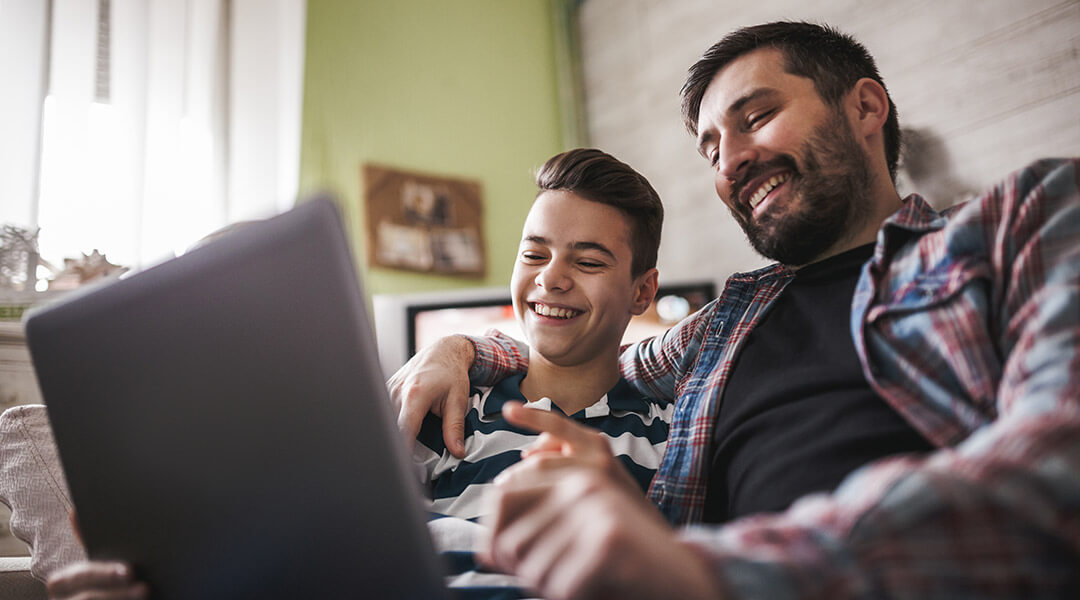 A smiling adult and teen looking at a laptop together.