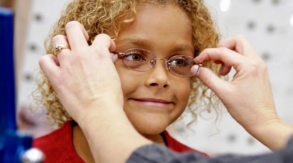 Adult fitting a pair of glasses on a child.