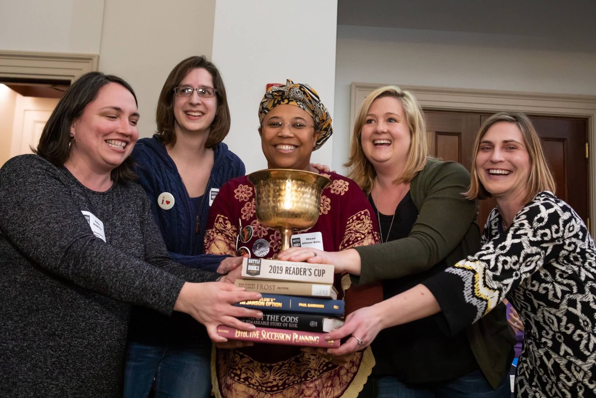 Five adults holding stack of books and trophy from Adult Battle of the Books event.