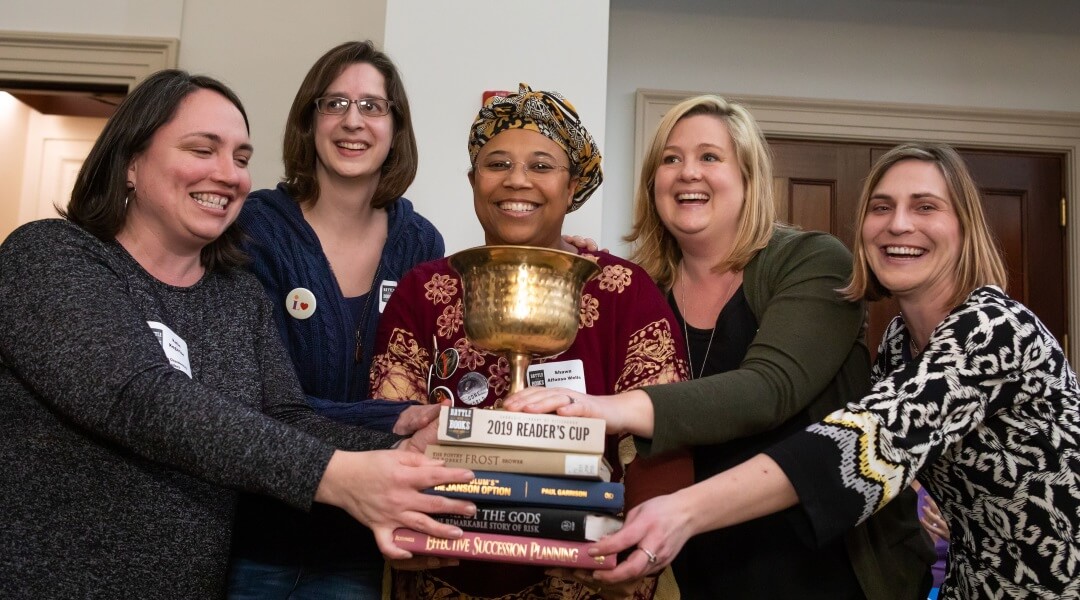 Five adults holding stack of books and trophy from Adult Battle of the Books event.