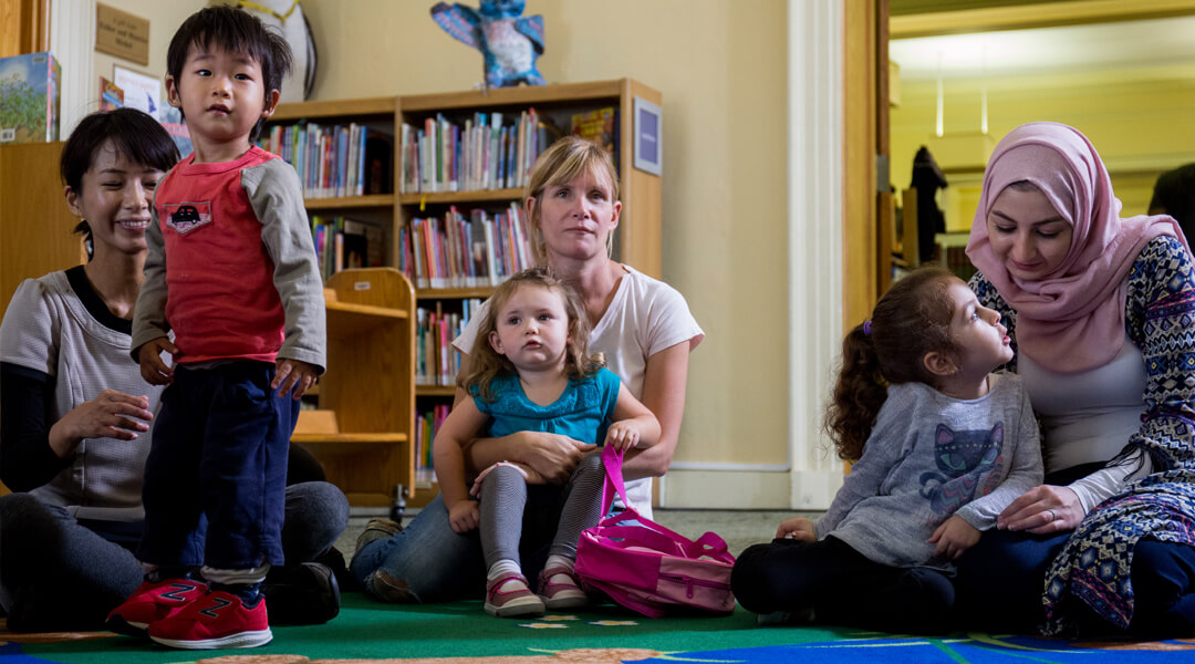 Toddlers and caregivers sit on floor for storytime